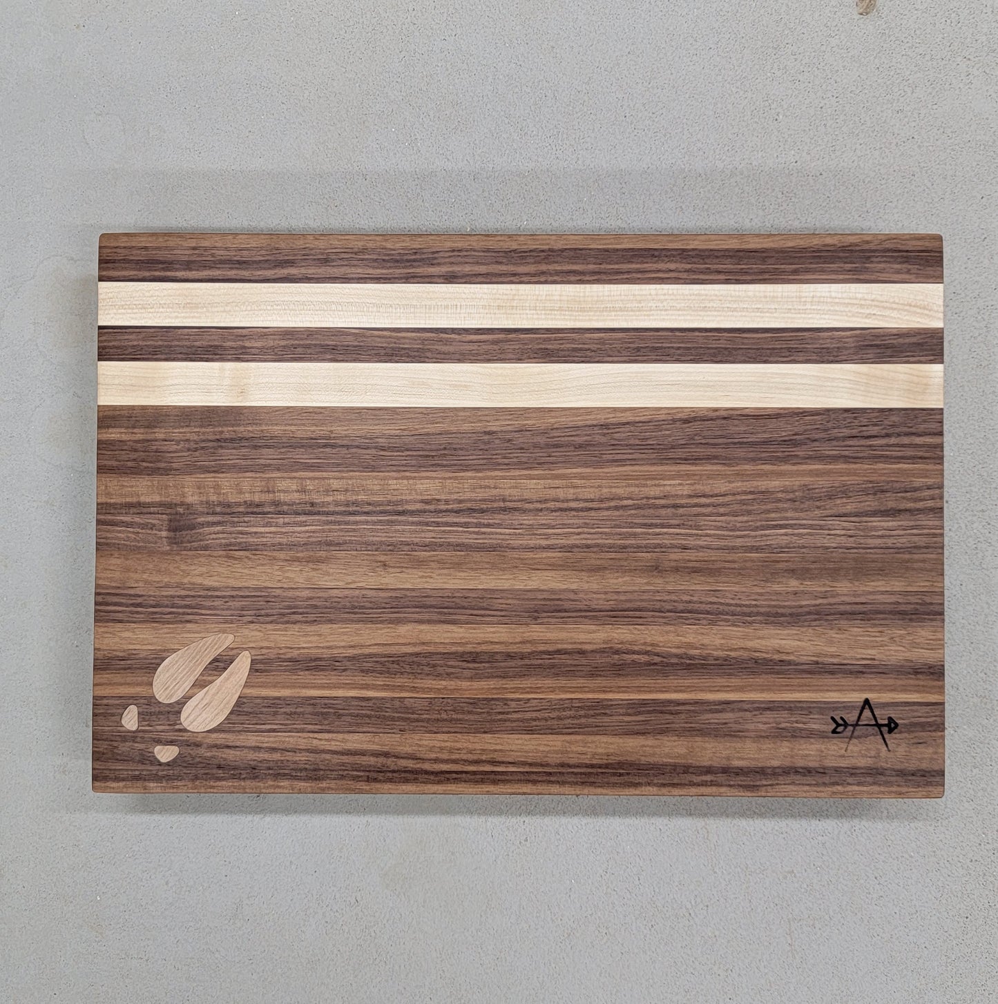 " Elk " Walnut and Maple Wood Cutting board

Artist: Kevin Shimkus

Edge-grain cutting board made of walnut and maple

Elk footprint inlay in lower left corner

Two maple stripes at the top of board

Has four small feet on bottom side of cutting board to prevent slipping

12" wide by 18" long by 2" deep

8.5 lbs