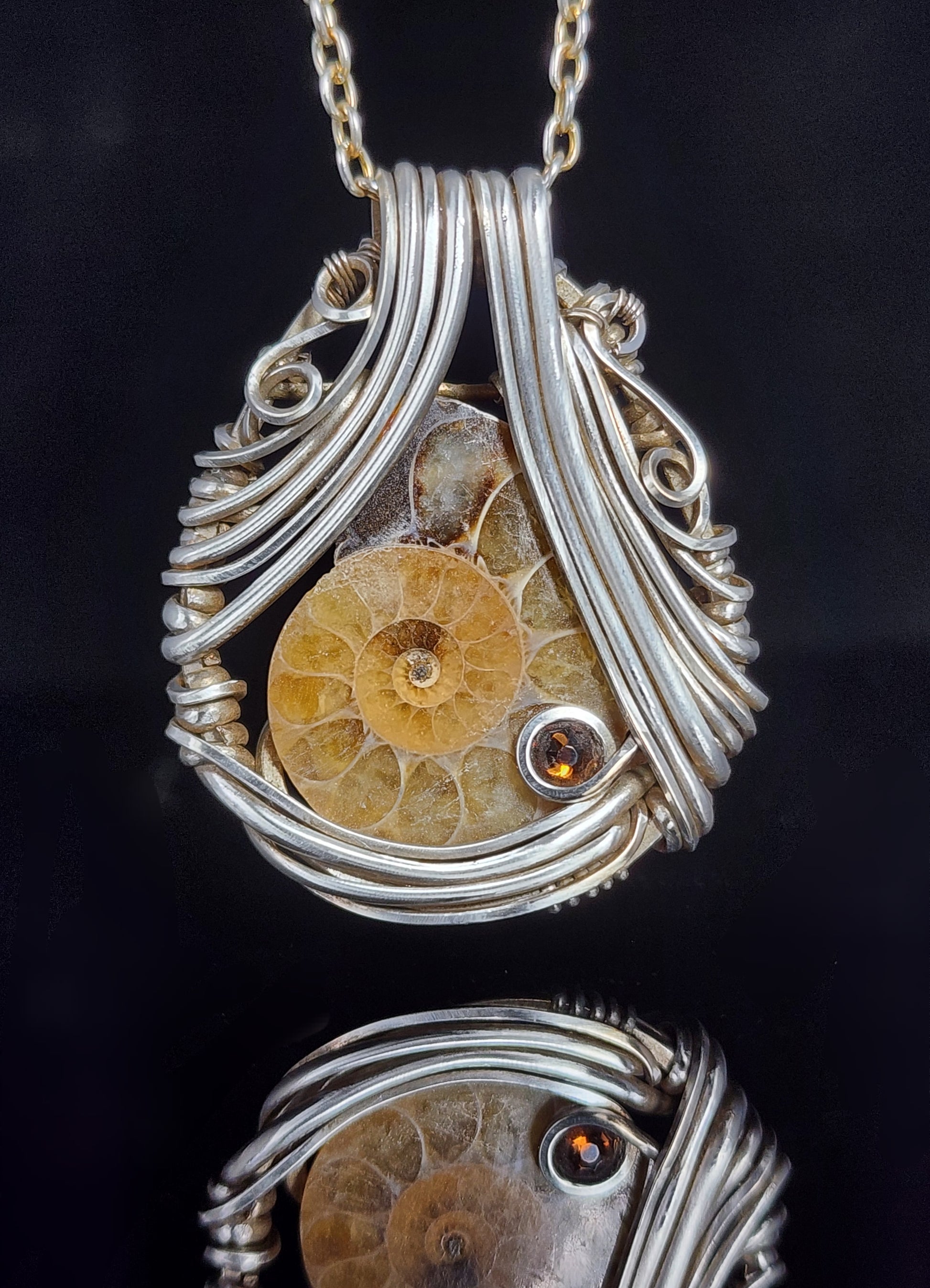 Ammonite Pendant  Artist: Lindsey Griffin&nbsp;   Ammonite&nbsp; sliced fossil wrapped in&nbsp; sterling silver wire   Swarovski crystal  Black cord 16" long   1 1/2" long x 1 1/4" wide 1/4" deep pendant  Comes with care instructions and cleaning cloth