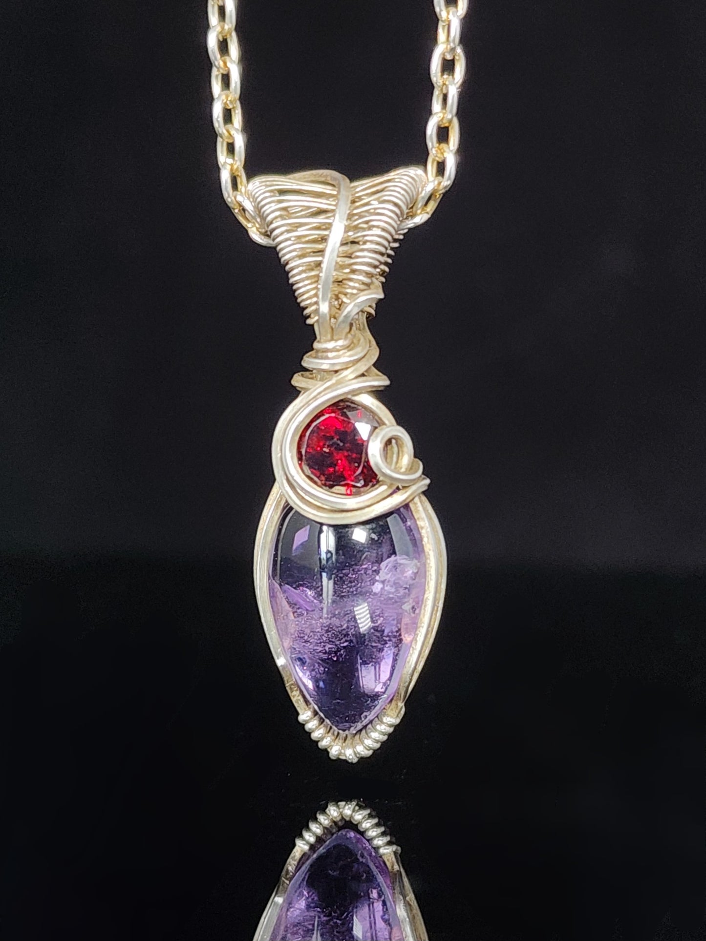 Amethyst and Garnet Wire Wrapped Pendant  Artist: Lindsey Griffin&nbsp;   Amethyst and&nbsp; faceted garnet in wrapped&nbsp; sterling silver  16" silver plated snake chain   1 3/8" long x 3/8" wide 1/4" deep pendant  Comes with care instructions and cleaning cloth